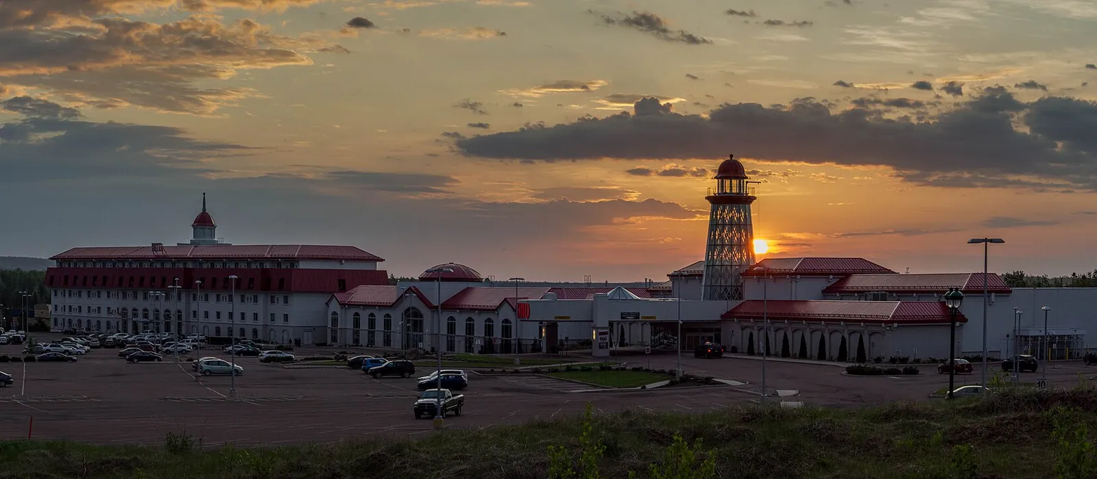 Casino Nouveau-Brunswick à Moncton au coucher du soleil : le bloc de l'hôtel, les ailes du casino aux toits rouges et la tour en forme de phare au-delà du stationnement